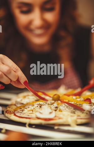 Primo piano di una giovane donna sorridente che mette la paprika sulla pasta per pizza. Foto Stock