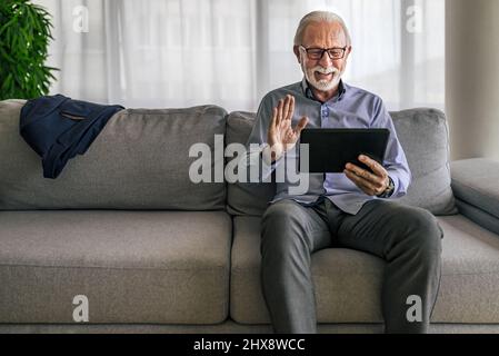 Sorridente allegro uomo anziano felice ondeggiante e gesturante a fotocamera che hanno una videochiamata online sul dispositivo portatile portatile tablet portatile portatile portatile portatile parlare con e collegare Foto Stock