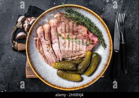 Cena barbecue - bistecche di maiale di carne al collo in piatto con le erbe. Sfondo nero. Vista dall'alto Foto Stock