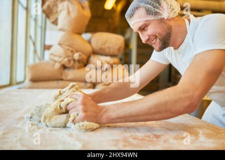 Panettiere giovane apprendista impastare l'impasto con la farina come preparazione in panetteria Foto Stock