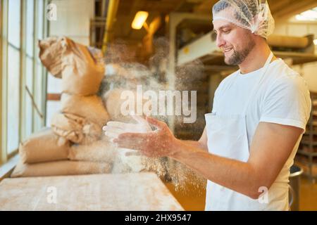 Il giovane uomo come apprendista panettiere spezza la farina dalle mani mentre impasta l'impasto in panetteria Foto Stock