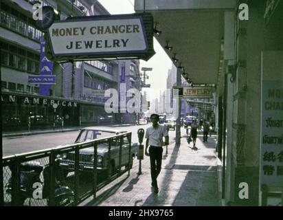 Scena stradale, uomo che cammina sul marciapiede di fronte a un punto di cambio valuta, in una città asiatica non identificata (possibilmente Giappone o Vietnam) alla fine del 60s o all'inizio del 1970s) Foto Stock