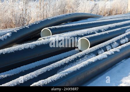 Tubi dell'acqua in plastica. Tubi in PVC nero tubi in plastica impilati su sfondo bianco di neve. Riparazione dell'alimentazione idrica. Riscaldamento case in inverno. Casa Foto Stock