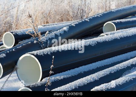 Tubi dell'acqua in plastica. Tubi in PVC nero tubi in plastica impilati su sfondo bianco di neve. Riparazione dell'alimentazione idrica. Riscaldamento case in inverno. Casa Foto Stock