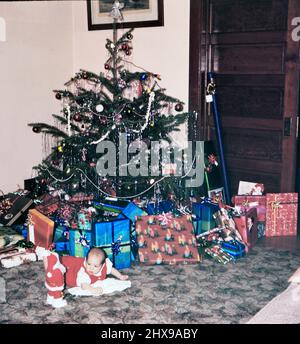 Bambino sdraiato di fronte ad un albero di Natale circondato da regali ca. 1965 Foto Stock