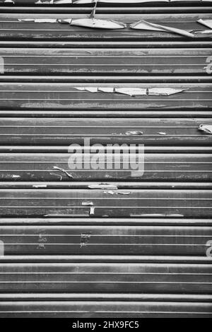 Sfondo grigio neutro di una serranda di un locale commerciale chiuso in cui rimangono resti di carta Foto Stock