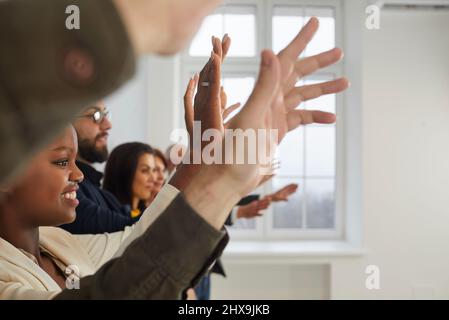 Un pubblico felice e diversificato che solleva le mani per porre domande durante la presentazione o il seminario Foto Stock