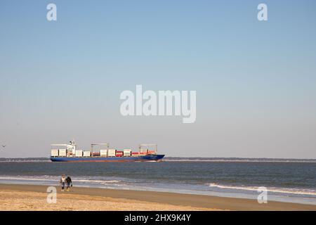 Tybee Island, Georgia, USA - 19 febbraio 2022 : nave container carico al largo della costa di Tybee Island, Georgia, con i turisti che camminano sulla spiaggia. Foto Stock