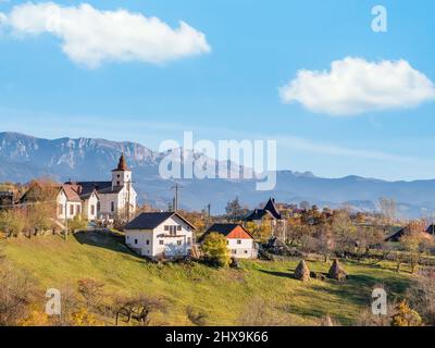 Bellissimo paesaggio rustico nel villaggio di Magura, in Romania, con case tradizionali rumene, una chiesa e le montagne Piatra Craiului sullo sfondo Foto Stock