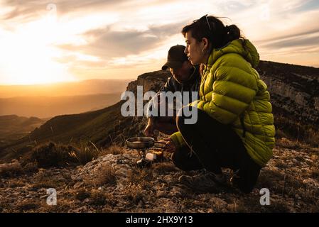 Giovane coppia di cucina durante un campeggio in montagna. Foto Stock