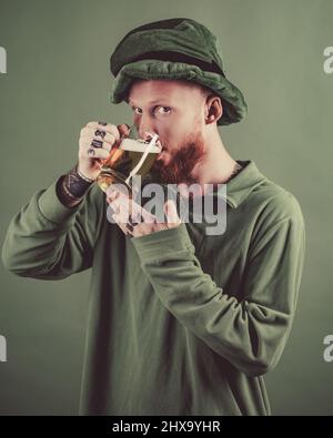 Fascino fortunato su sfondo verde. Cappello di leprechauns. L'uomo su sfondo verde festeggia il giorno di San Patrizio. Ritratto di uomo eccitato che tiene un bicchiere di birra sopra Foto Stock