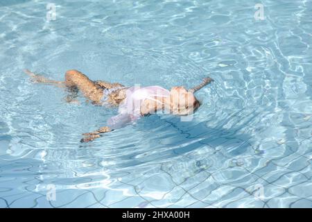 Bella donna bionda che galleggia sulla schiena in una piscina Foto Stock