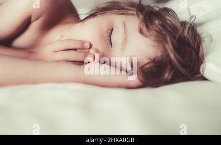 Bambini piccoli che dormono con la bocca aperta, russando. I bambini in camera dormono sul letto con lenzuola bianche e cuscini. Foto Stock