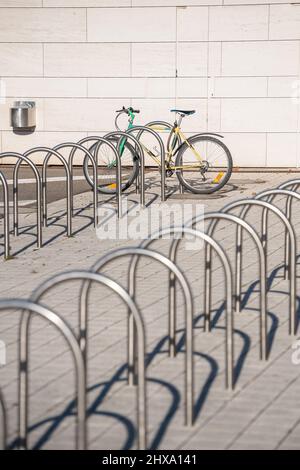 Rack vuoti multipli in acciaio inossidabile fissati per biciclette, progettati per parcheggiare le biciclette nell'area urbana della città - una bicicletta parcheggiata sullo sfondo Foto Stock