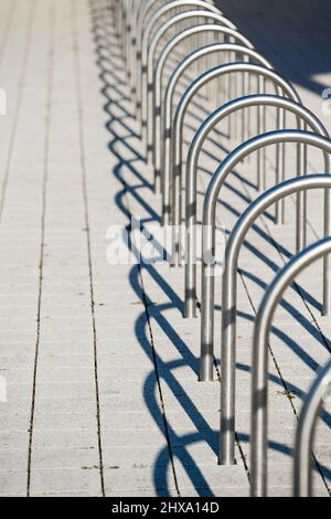 Immagine verticale Vista in prospettiva di più cavalletti vuoti in acciaio inossidabile fissati con le sue scaffalature vuote ombre progettate per parcheggiare le biciclette nell'area urbana della città Foto Stock