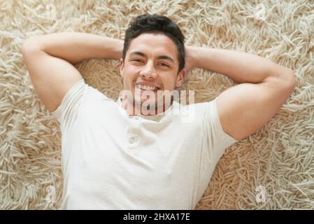 È il momento di ottenere dolce. Ritratto di un giovane felice che si rilassa sul tappeto a casa. Foto Stock