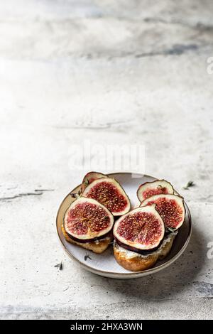 Due panini con fichi, formaggio, timo e miele sul piatto su sfondo testurizzato. Spazio di copia. Orientamento verticale Foto Stock