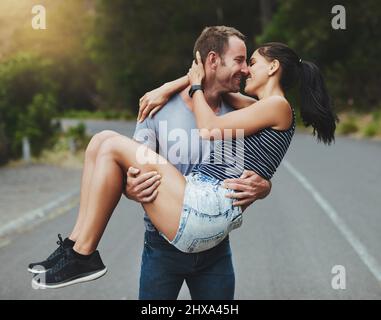 Youre il mio cavaliere in armatura luminosa. Sparato di un giovane uomo che porta romanticamente la sua ragazza lungo una strada all'aperto. Foto Stock