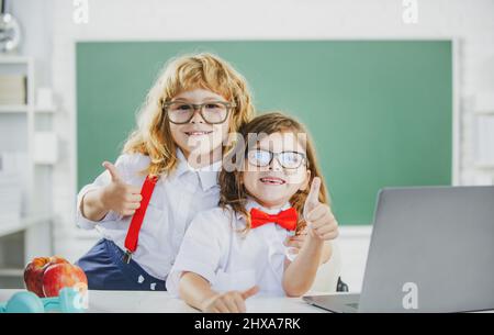 Amici della scuola. Due ragazzi della scuola, ragazza carina e ragazzo con i pollici a scuola vicino alla lavagna. Foto Stock