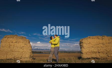 Uomo e donna in abbigliamento sportivo giallo verde. Una coppia incantevole di viaggiatori si abbraccia e bacia vicino alla pietra vecchia godendo il paesaggio delle Highland. Due viaggiatori sono Walkin Foto Stock