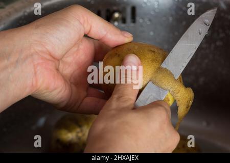 Donna mano pelando la patata nel lavandino con il coltello ordinario Foto Stock