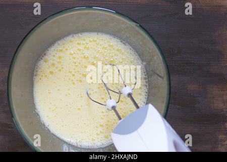 Miscelatore manuale donna nel recipiente di vetro con zucchero e uova che battono Foto Stock