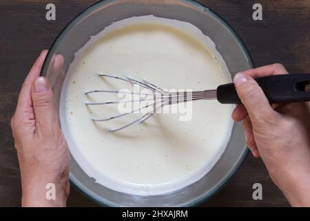 La donna che tiene la mano sussurra nel recipiente di vetro mentre sbatte le uova Foto Stock