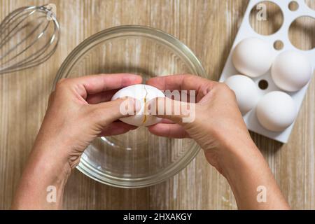 Mano di una donna che tiene l'uovo crudo rotto prima di battere per aprirlo e separarlo Foto Stock