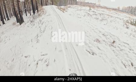 Vista POV. Stabilizzazione gimbal portatile. Motociclista sportivo professionista che guida una bici grassa all'aperto. Giro in ciclista nella foresta di neve d'inverno. M Foto Stock