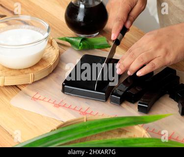 Donna mano tagliata a fette Cincau Hitam o Black Grass Jelly Pudding in pezzi Cube, sano concetto di cibo Foto Stock