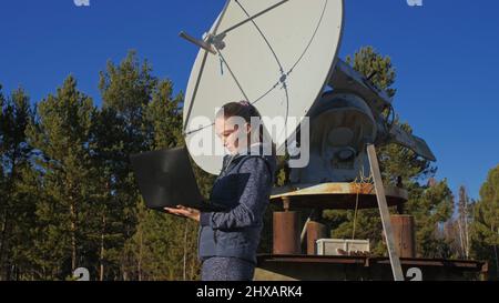 Donna studente operatore di Istituto di fisica solare terrestre monitora le apparecchiature di comunicazione in notebook. Cannocchiale radio solare a schiera unico. Dom
