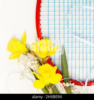 Tennis. Composizione sportiva per le vacanze con racchetta da tennis con bouquet di narcisi su sfondo bianco. Sport e stile di vita sano. Il concetto di outd Foto Stock