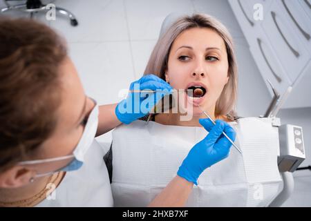 Dentista e paziente nell'ufficio dentistico. Donna caucasica alla nomina del medico, il medico effettua un esame e un trattamento dentale Foto Stock