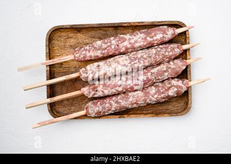 Salsicce di manzo crudo non cotti e kebab di carne di agnello, su sfondo tavola di pietra bianca, vista dall'alto piatto Foto Stock