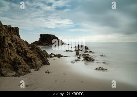 Una lunga esposizione di una piccola spiaggia pittoresca in una baia rocciosa con barriera corallina a bassa marea Foto Stock