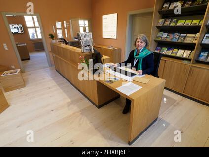 11 marzo 2022, Brandeburgo, Caputh/Schwielowsee: Marion Trumbull, responsabile della cultura e del turismo, siede al banco della reception della casa di alloggio ristrutturata del castello di Caputh. Il Caputh Palace è il più antico palazzo del piacere rimasto dai tempi del Grande Elettore Federico Guglielmo di Brandeburgo nel paesaggio culturale di Potsdam. Come edificio annesso, la Logierhaus confina con il cortile del palazzo ed è ora nuovamente aperta ai visitatori. Parte dell'edificio della Fondazione dei palazzi e dei giardini prussiani (SPSG) è ora utilizzato dall'ufficio informazioni turistiche del comune di Schwielowsee. Foto: S Foto Stock