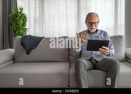 Sorridente allegro uomo anziano felice ondeggiante e gesturante a fotocamera che hanno una videochiamata online sul dispositivo portatile portatile tablet portatile portatile portatile portatile parlare con e collegare Foto Stock