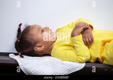 Una bambina afroamericana in abito giallo si trova sul pavimento e sorride. Foto Stock