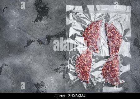 Cotolette di vitello di manzo in confezione di plastica sottovuoto, su sfondo grigio del tavolo in pietra, con vista dall'alto, con spazio per la copia del testo Foto Stock