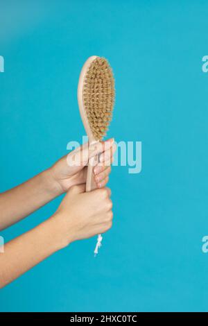 Mani femminili con spazzola per massaggio secco della pelle in legno su sfondo blu. Procedure anticellulite che mirano a sbarazzarsi della cellulite. Auto Foto Stock