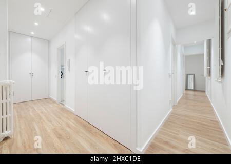 Corridoio di una casa residenziale con pavimenti in legno duro, legno bianco su porte e finestre, e pareti dipinte di bianco, legno-incorniciata specchio, e ghisa-ferro ra Foto Stock