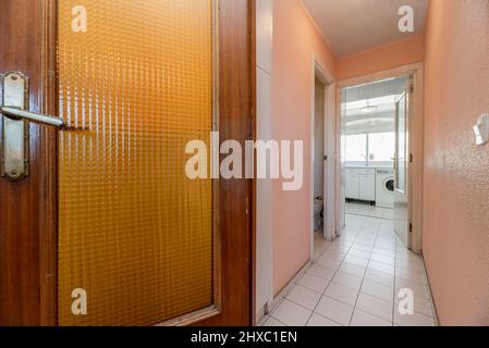 Porta in legno e vetro in corridoio con pavimenti in gres bianco e pareti dipinte di rosa Foto Stock