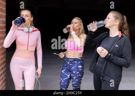 Sport belle donne giovani di diversi tipi di corpo bere acqua dalla bottiglia dopo aver allenato fuori da una palestra, palestra, fitness, concetto sportivo . Foto di alta qualità Foto Stock