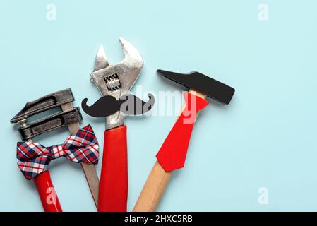 Felice Festa del Padre. Vista dall'alto degli strumenti di lavoro con bow tie, baffi falsi e cravatta su sfondo blu. Concetto di festa del Padre Foto Stock