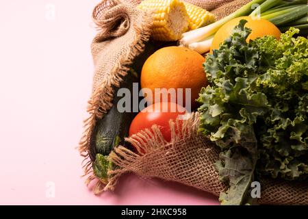 Primo piano di kale, frutta, zucchine, scalpello e cornetti su sfondo rosa Foto Stock