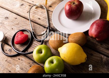 Vista ad angolo alto di vari frutti con stetoscopio e forma a cuore su tavola di legno Foto Stock