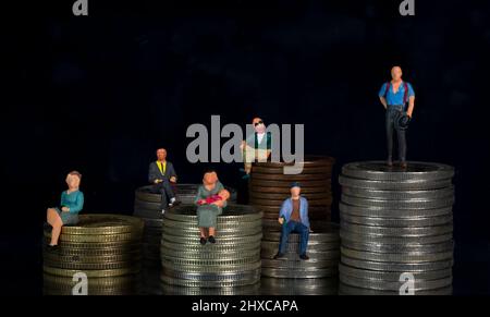 Persone in miniatura su pile di diverse altezze di monete. Concetto di reddito e disuguaglianza economica sfondo nero Foto Stock