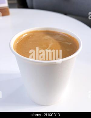 Espresso con latte e schiuma di tigre in una tazza di carta usa e getta su un tavolo bianco Foto Stock