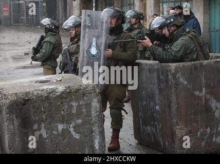 Hebron. 11th Mar 2022. Un soldato israeliano punta la sua arma contro i manifestanti palestinesi durante gli scontri a seguito di una protesta contro l'espansione degli insediamenti ebraici nella città di Hebron, in Cisgiordania, il 11 marzo 2022. Credit: Mamoun Wazwaz/Xinhua/Alamy Live News Foto Stock