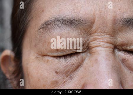 Rughe intorno ad occhio chiuso della donna anziana asiatica. Primo piano. Foto Stock